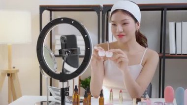 Genç Asyalı kadın kozmetik ürünlerini sosyal medya platformunda takipçiler, krem ya da losyonu canlı yayında inceleyen, etkileyen ve gözden geçiren kadınlar için heyecan verici bir şekilde sunup gözden geçiriyor..