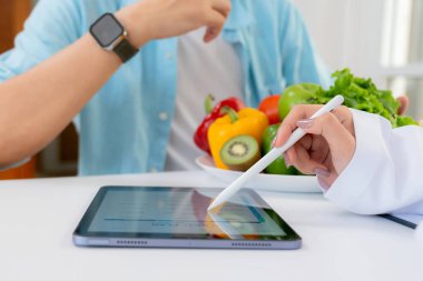 Asyalı beslenme uzmanı, AI ile kişiselleştirilmiş yemek planını sağlık hizmetleri danışmanlığı sırasında hastaya açıklamak için tablet kullanıyor, sağlıklı yaşam tarzı, kadın diyetçisi, tablette yapay zekayla beslenme planı gösteriyor..
