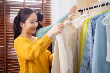 Hazırlık teslimatı için mağazada kıyafet düzenleyen iki genç Asyalı kadın, satıcı seçici giysiler, perakende satış için seçici giysiler, teslimat için mal, küçük işletme.
