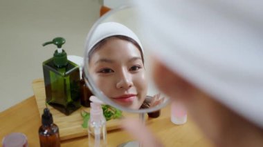 Evdeki oturma odasında kırışıklıkları kontrol etmek için aynaya bakan genç Asyalı güzel bir kadın, nemlendirici süren mutlu bir kadın. Hijyen, cilt bakımı, cilt bakımı, cilt bakımı ve cilt bakımı..