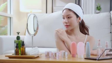 Güzel, genç Asyalı bir kadın, oturma odasında aynaya bakarken krem ya da losyon sürüyor. Omzunda, cildinde ve sağlığında gençleşme için cilt bakımı yapan mutlu, güzel bir kadın..