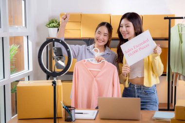 İki Asyalı kadın online giyim mağazasında canlı yayın yaparken sosyal ve başarılı giysiler sergiliyorlar. Girişimci çevrimiçi giyim ve sunum için internetten yayın yapıyor..