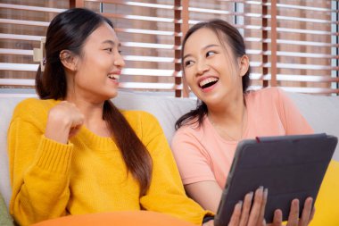 Oturma odasında dijital tablet kullanan iki genç Asyalı kadın, sosyal medyayı internet tableti ve konuşma mesafesi için kullanan kadın, yaşam tarzı kavramı.