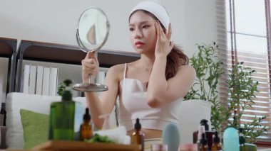 Genç Asyalı kadın, yüz bakımı stresi ile aynaya bakıyor. Oturma odasındaki kanepede oturuyor. Cilt bakımı, cilt bakımı, cilt bakımı, cilt bakımı ve cilt bakımı..