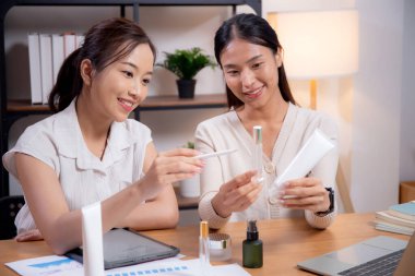 Ofiste kozmetik ürünü ya da kremi test eden ve araştıran iki Asyalı iş kadını. Cilt tasarımı, geliştirme ve iş dünyasından iki iş kadını..
