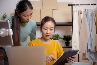 Tablet üzerinde çalışan iki genç Asyalı kadın çevrimiçi işleri yönetir ve planlarken ve evde siparişleri kontrol ederken, girişimci ve küçük işletme, çevrimiçi satıcı ile perakende satış, girişim işi.