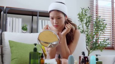 Genç Asyalı kadın, yüz bakımı stresi ile aynaya bakıyor. Oturma odasındaki kanepede oturuyor. Cilt bakımı, cilt bakımı, cilt bakımı, cilt bakımı ve cilt bakımı..