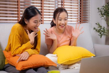 Kanepede oturan iki genç Asyalı kadın evdeki oturma odasında dizüstü bilgisayar kullanıyor, sosyal medyayı internet ve sohbet için kullanıyor, yaşam tarzı kavramı..