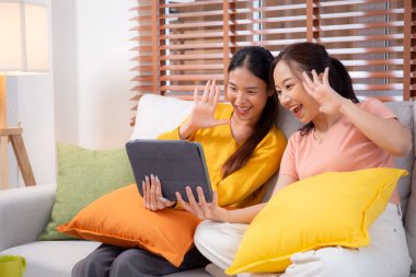 Oturma odasında dijital tablet kullanan iki genç Asyalı kadın, sosyal medyayı internet tableti ve konuşma mesafesi için kullanan kadın, yaşam tarzı kavramı.