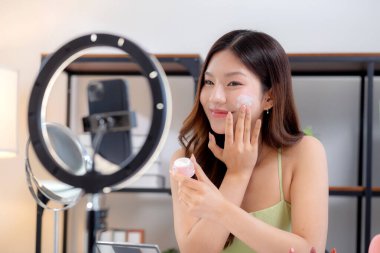 Genç Asyalı kadın kozmetik ürünlerini sosyal medya platformunda takipçiler, krem ya da losyonu canlı yayında inceleyen, etkileyen ve gözden geçiren kadınlar için heyecan verici bir şekilde sunup gözden geçiriyor..