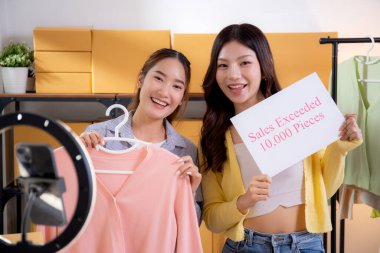 İki Asyalı kadın online giyim mağazasında canlı yayın yaparken sosyal ve başarılı giysiler sergiliyorlar. Girişimci çevrimiçi giyim ve sunum için internetten yayın yapıyor..