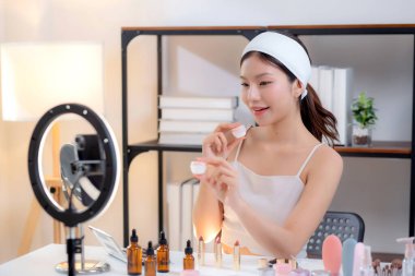 Genç Asyalı kadın kozmetik ürünlerini sosyal medya platformunda takipçiler, krem ya da losyonu canlı yayında inceleyen, etkileyen ve gözden geçiren kadınlar için heyecan verici bir şekilde sunup gözden geçiriyor..