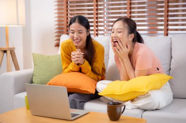 Kanepede oturan iki genç Asyalı kadın evdeki oturma odasında dizüstü bilgisayar kullanıyor, sosyal medyayı internet ve sohbet için kullanıyor, yaşam tarzı kavramı..