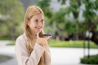 Kafkasyalı genç iş kadını akıllı telefonda sohbet robotu ya da açık havada yapay zeka ile sesli mesaj kullanıyor iş kadını, akıllı telefonla konuşan şehir yapay zekası olan ses asistanı Al ile konuşuyor..