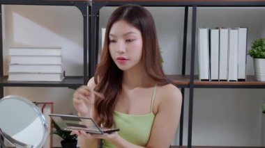 Yanağına bir ayna, güzellik ve kozmetik ile makyaj yapan mutlu, genç Asyalı bir kadın güzel, rahat bir yaşam tarzı, tatmin olmuş ve kozmetolojisi olan bir kadın..