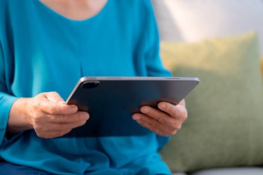 Ev oturma odasında tablet okuyan son sınıf öğrencisi kadın, çevrimiçi bağlantı ve dijital yaşam tarzı, sosyal medya için tablet izleyen yaşlılar, uzaktan öğrenme, sohbet robotu ya da yapay zeka kullanan yaşlılar.