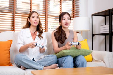İki Asyalı kadın, evdeki rahat bir oturma odasında bilgisayar oyunu oynuyorlar. Eğlence, arkadaşlık ve neşeli bir yaşam tarzı. Asyalı arkadaşlar, eğlence ve oyun paylaşımının keyfini çıkarıyorlar..