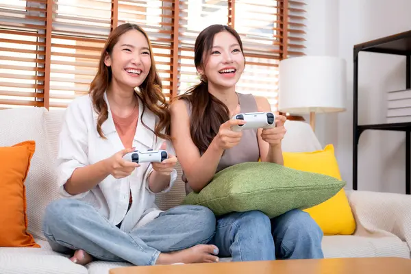 İki Asyalı kadın, evdeki rahat bir oturma odasında bilgisayar oyunu oynuyorlar. Eğlence, arkadaşlık ve neşeli bir yaşam tarzı. Asyalı arkadaşlar, eğlence ve oyun paylaşımının keyfini çıkarıyorlar..