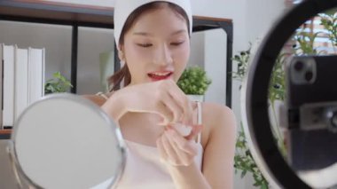 Sosyal medyada kozmetik ürünü sunan ve gözden geçiren Asyalı genç bir kadın, cilt kremi ürünlerini telefonla, canlı yayında ya da yayında inceleyen güzellik uzmanı, içerik yaratıcısı.