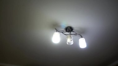 Odada güzel bir avize. Otel odasında avize var. Beyaz tavanda bir avize asılı. Şüpheliyi yakın plan çekiyoruz. Tavanda modern kristal avize