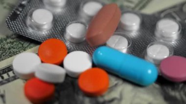 Bir yığın farklı renkli hap ve kapsül Amerikan dolarları üzerinde yatar ve döner. Pahalı tıp, eczacılık, ilaç endüstrisi, tedavi maliyeti konsepti ve sağlık sigortası.