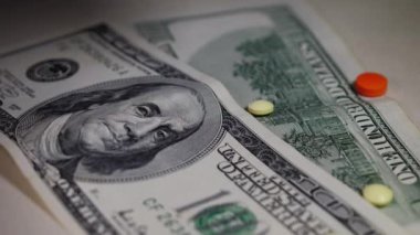 Amerikan dolarlarına düşen farklı renkli haplar, ağır çekimde. Pahalı tıp, eczacılık, ilaç endüstrisi, tedavi maliyeti konsepti ve sağlık sigortası. Tedavinin yüksek maliyeti.