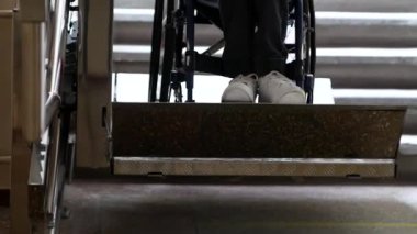 A disabled young man in a wheelchair ascends on an automatic electric ramp. Close up of wheelchair wheel and disabled person's legs.