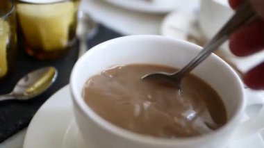 Close-up cup with coffee. A man's hand holds a teaspoon and stir the Americano coffee with milk.