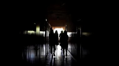 A crowd of women are walking along the old long corridor. The outlines of the girls in the long hall. Backlit people walking in front. Back light. Slow motion video of women silhouettes.