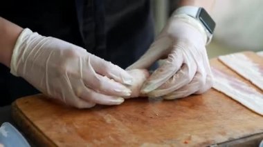 Chef makes rolls  with bacon and banana on the dark wooden board in the kitchen, close up shot of cooking meat for grilling