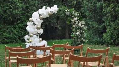 Çok sayıda kahverengi ahşap sandalye düğün dekorunun arka planına karşı dizilmiştir. Düğün kemerinin arka planında konuklar için boş koltuklar.