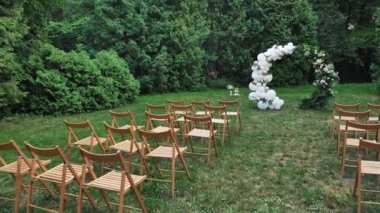 Çok sayıda kahverengi ahşap sandalye düğün dekorunun arka planına karşı dizilmiştir. Düğün kemerinin arka planında konuklar için boş koltuklar.