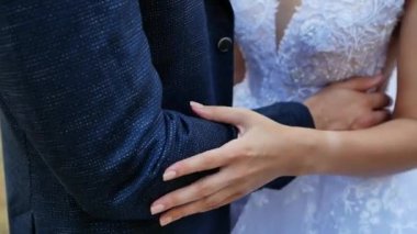 Yakın çekim, güneşli güzel bir yaz gününde, yeni evlilerin elleri birbirlerini okşarlar. Birbirini seven yeni evliler sarılıyorlar..