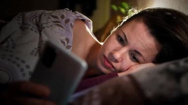 Genç Avrupalı kadın yatakta yorgun, evde cep telefonuyla mesajlaşıyor. Yatak odasında cep telefonu olan beyaz bir kız. İnsanlar uykusuzluk çekerken akıllı telefon kullanıyor. Yatmadan önce bir alet kullanıyorsun.