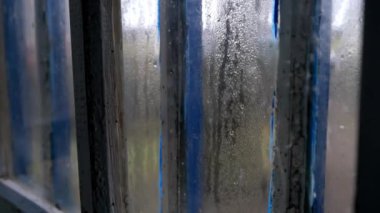 Yağmur damlaları eski, harap bir pencerenin camından aşağı akıyor. Yağmurlu havanın eski bir pencerenin içinden eski püskü bir boyayla görüntüsü..