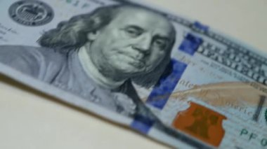 Makro video çekimi. 100 dolarlık banknotun masadan kayarak geçişi. Çerçevede 100 dolar beliriyor ve sonra kayboluyor. George Washington, ABD banknotunda. Para ve finans, nakit..