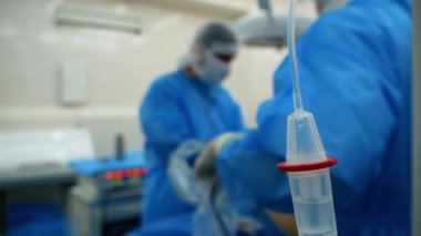 Damar içi ilaç infüzyon sisteminin izole edilmiş damlatıcısını bir cerrah ekibinin arka planına karşı kapatın. Kanser tümörünü almak için ameliyat sırasında serum verin. Hastanedeki ameliyathanede.. 