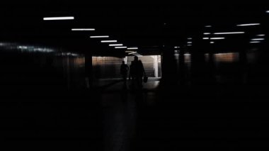 Arka plandaki kalabalık alt geçit boyunca yürüyor. Yayalar gün ışığına karşı metronun merdivenlerinden inip çıkıyorlar. Şehir hayatı ve koşuşturma. İnsanların gölgeleri
