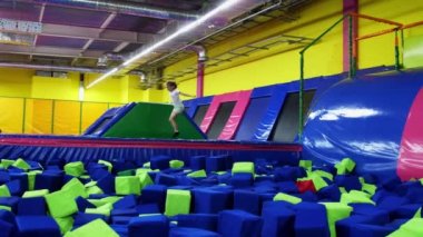 Neşeli genç bir kız trambolinde zıplıyor sonra da yumuşak oyuncak küpleriyle havuza atlıyor. Neşeli bir çocuk, çocuk eğlence merkezinde zevkle oynar. Çocuklar eğlenir.