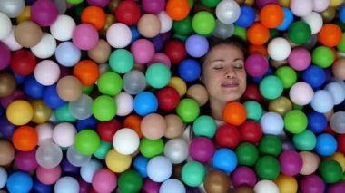 Güzel kız renkli plastik toplarla dolu bir havuzda yatıyor. Mesajlaşma yeri, kızla neşeli bir video. Gülümseyen beyaz kadın gözlerini açar ve kameraya bakar. Bir sürü küçük topun arasında..