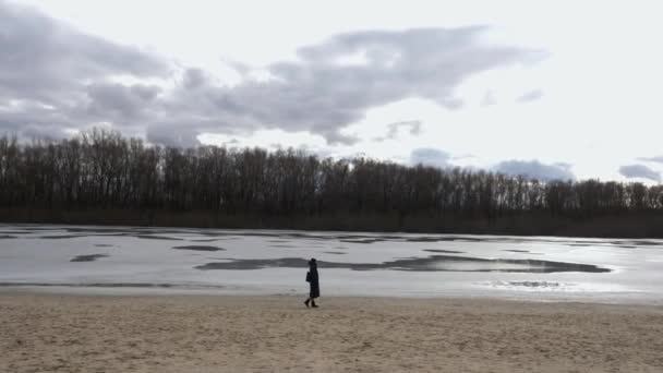 一个女孩在一条冰冻的河流的背景下沿着冬季的海滩散步 在一个凉爽的早晨 在早春散步 在新鲜空气中散步时的宁静 放松和与大自然的团结 — 图库视频影像