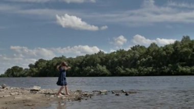 Elbise giymiş küçük bir kız çocuğu güneşli bir yaz gününde sahilde suda oynar. Tasasız çocukluk