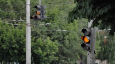 Arka planda iki trafik ışığı var. Yanıp sönen yeşil bir trafik ışığı önce sarıya sonra da kırmızı ışığa geçer. Bir şehir yolunda düzenli kavşak.