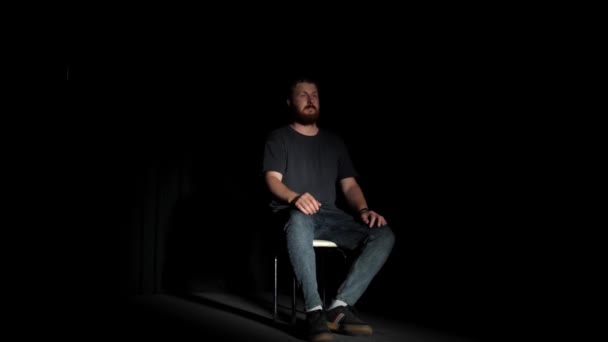 Ένας Γενειοφόρος Κάθεται Σκεπτικά Μια Καρέκλα Ένα Σκοτεινό Δωμάτιο Φωτισμένο — Αρχείο Βίντεο