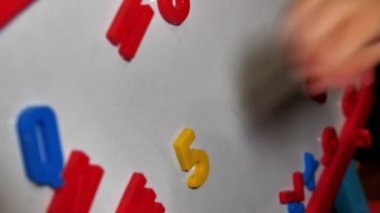 Küçük kız uzaktayken evde matematik öğreniyor. Matematiksel bir problemi çözen bir anaokulu kızının ellerine yakın çekim. Ya da bir tahtaya mıknatıs numarası koyarak bir örnek..