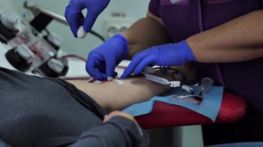 Bir hemşire, kan bağışı sırasında bir kadının kolundaki damar ya da atardamardaki kateteri çıkarır. Bir doktor, analiz için kan almak için hastanın damarını iğneyle deler..