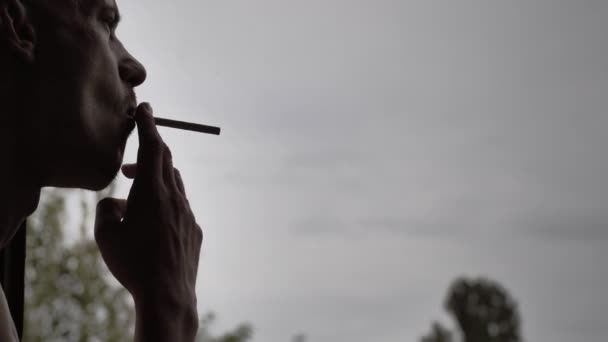 담배에 붙이고 담배를 천천히 피우는 남자의 배경에 불이켜 필멸자가 구름낀 — 비디오
