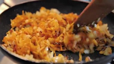 Ev mutfağında yemek pişirmek. Aşçı, ahşap bir spatulayla karıştırılmış tavada soğanlı haşlanmış havuç hazırlıyor. Çorba ya da makarna için havuçlu soğan kızartıyorum..