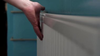 Bir adam ısıtma sisteminin radyatör bataryasını eliyle kontrol eder. Soğuk kışta odayı ısıtıyor. Enerji verimli ısı iletişimi.
