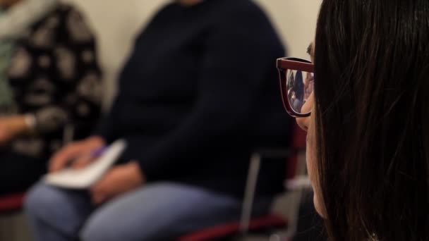 大学での授業や研修で眼鏡をかけた女の子のクローズアッププロフィール 女の子は集団イベント中に注意深く耳を傾ける — ストック動画